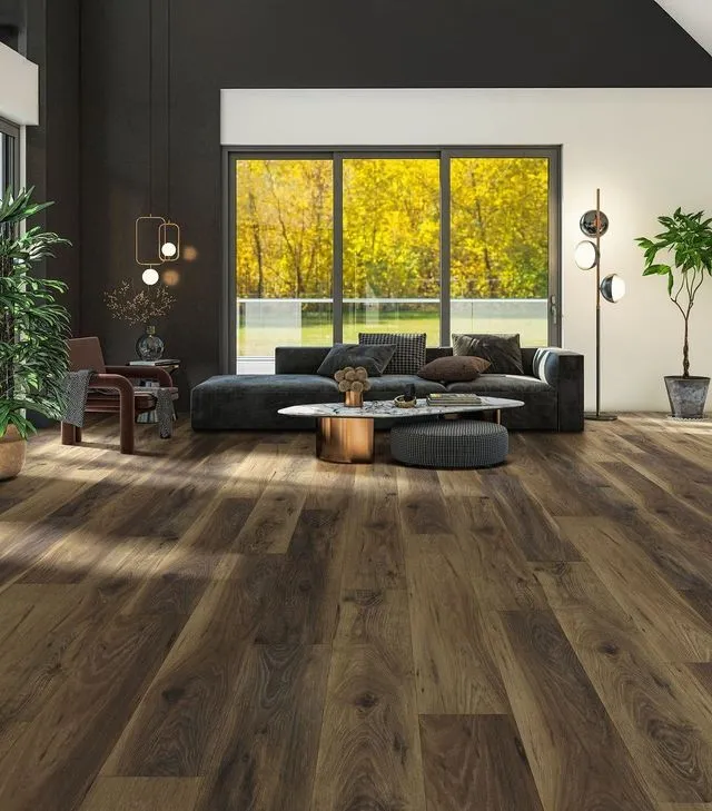 A modern living room with hardwood floors, a dark sofa, a coffee table, and large windows overlooking autumn trees.